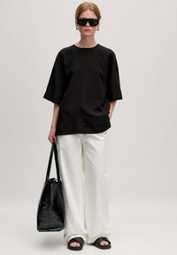 Zwarte oversized t-shirt met korte mouwen, witte wijde broek, zwarte sandalen en een zwarte tote bag. Glad materiaal met een minimalistisch ontwerp.