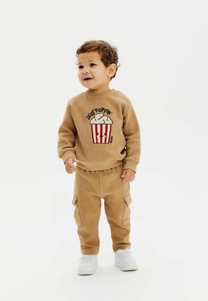 Sudadera de punto waffle color bronce, con un gráfico de palomitas, combinada con pantalones cargo a juego. Incluye cinturilla elástica y zapatillas blancas.