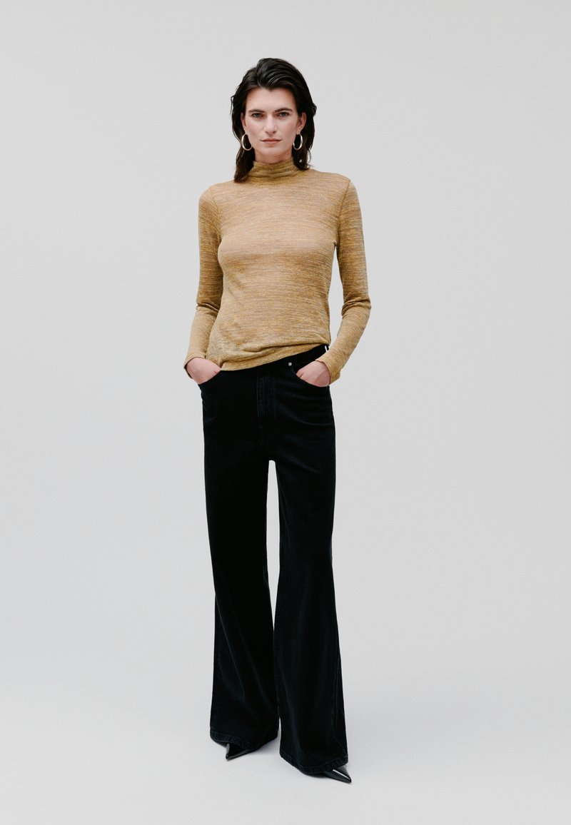 Mustard long-sleeve top with mock neck, paired with high-waisted black flared pants, featuring front pockets and smooth texture.