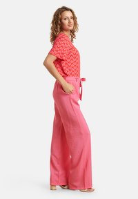 Rotes gemustertes Oberteil mit kurzen Ärmeln, kombiniert mit weit geschnittenen rosa Hosen mit einem Bindeband in der Taille. Leichter Stoff und lockere Passform.