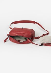 Red leather crossbody bag with a rectangular shape, single adjustable strap, zipper closure, and a beige striped inner lining.