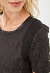 Vestido negro con un patrón texturizado de diseños geométricos, mangas lisas y un escote redondo con un ribete en contraste.