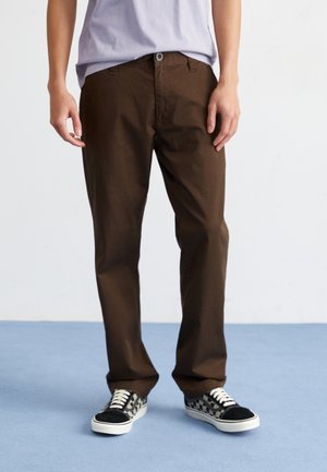 Pantalons en coton marron avec une coupe droite, poches avant et une fermeture à bouton unique, associés à des baskets noir et blanc à motifs.