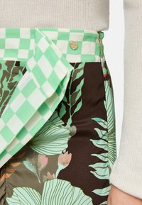 Rockmuster-Rock mit grünen und braunen Farbtönen, mit einem grün karierten Bund, goldenen Metallteilen und einem seitlichen Reißverschluss.