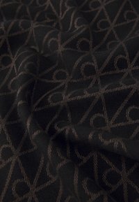 Schwarzer Stoff mit einem dezenten, filigranen braunen geometrischen Muster. Das Material hat eine weiche Textur und einen leichten Glanz, mit ineinander verwobenen Linien und Formen.