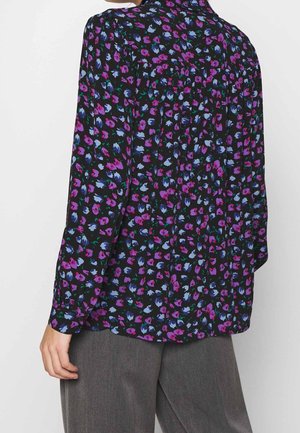 Person wearing a long-sleeve black blouse with small purple and blue floral print, paired with loose gray pants, seen from the back.