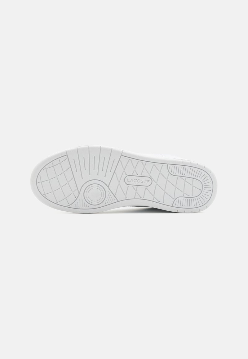 White sneaker sole with textured grip, featuring a circular emblem and the brand name "LACOSTE" printed centrally. Minimalist design.