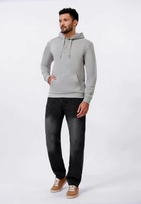 Γκρι φούτερ με κουκούλα, μπροστινή τσέπη, πουκάμισο με κουμπιά και κορδόνια, σε συνδυασμό με μαύρα τζιν και καφέ αθλητικά παπούτσια. Απλός και λειτουργικός σχεδιασμός.