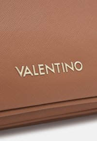 Portafoglio in pelle marrone con textura, caratterizzato da un logo 'Valentino' dorato embossato sulla parte anteriore, con una finitura liscia e una forma strutturata.