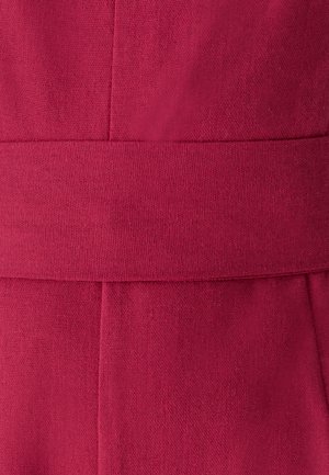 Zbliżenie teksturowanej tkaniny w głębokim różowym kolorze z poziomymi i pionowymi szwami tworzącymi pasek wzdłuż środka.