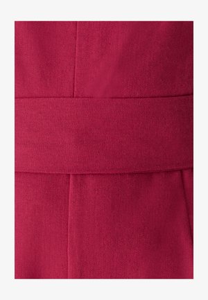 Lähikuva syvän vaaleanpunaisesta kankaasta, jossa on pystysuuntaiset ja vaakasuorat saumat muodostamassa vyömäisen nauhan keskelle.