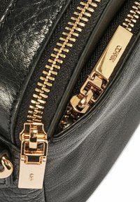 Czarna skórzana torba z złotymi akcentami, podwójnymi suwakami i teksturowaną powierzchnią. Zęby zamka są widoczne, co podkreśla elegancki design.