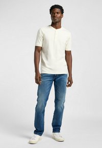Hvid kortærmet henley skjorte med rund hals og tre-knaps lukning, kombineret med blå denimjeans og hvide sneakers.