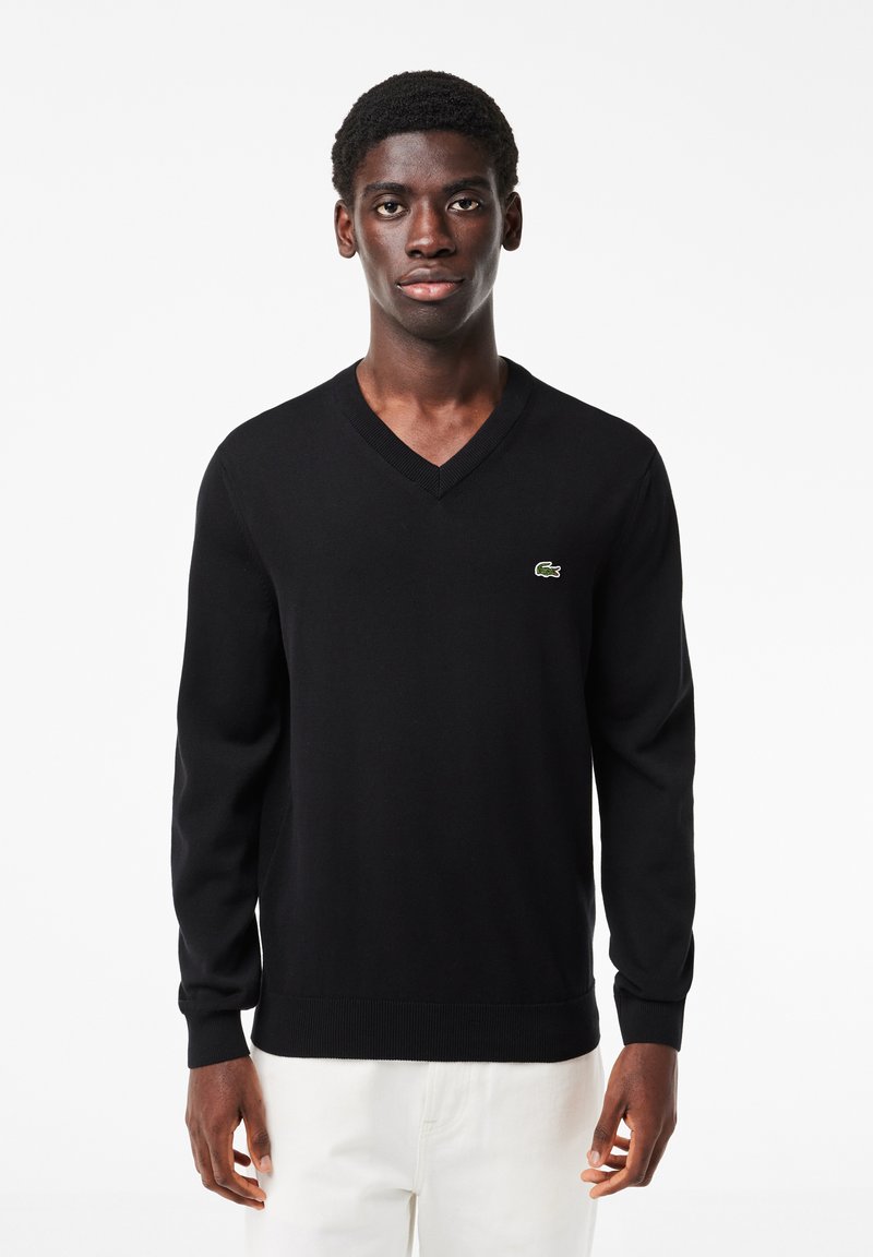 Maglione nero a scollo a V realizzato in tessuto morbido, con colletto e polsini a coste, impreziosito da un piccolo logo verde Lacoste sul petto.