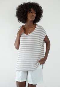 Lekko paskowany sweter w kolorze beżowym i białym, z dekoltem w kształcie litery V i krótkimi rękawami. Połączony z jasnymi, luźnymi szortami z miękkiego materiału.