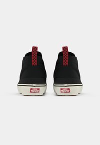 Pair of black Vans sneakers viewed from the back, featuring white soles, red checkerboard pull tabs, and red "Off The Wall" logo tags.