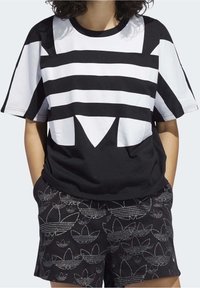 Svart- och vitrandig kortärmad t-shirt med en djärv geometrisk design, tillverkad av slätt tyg, ihop med mönstrade svarta shorts.