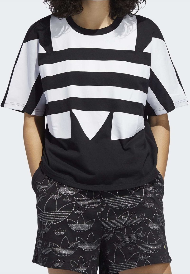 Svart- och vitrandig kortärmad t-shirt med en djärv geometrisk design, tillverkad av slätt tyg, ihop med mönstrade svarta shorts.