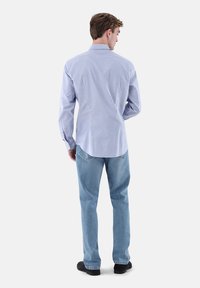 Gestreiftes Langarmhemd in Hellblau und Weiß, kombiniert mit hellen Jeans aus Denim. Das Hemd verfügt über einen geknöpften Kragen und eine lockere Passform.