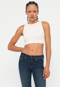 Λευκό ριμπ crop top με στρογγυλή λαιμόκοψη, συνδυασμένο με σκούρα μπλε τζιν στενής γραμμής. Το σύνολο διαθέτει απαλές υφές και εφαρμοστά σχέδια.
