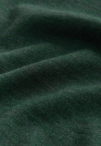 Mörkgrönt stickat tyg med en mjuk textur. Ytan visar ett jämnt mönster av fina stygn och subtila veck.