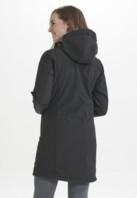 Mustapituinen pitkä takki hupulla, jossa on teksturoitu pinta, pystysaumat ja sivupaneelit muotoillun ilmeen saavuttamiseksi.