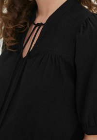 Blusa nera con maniche a sbuffo, caratterizzata da un collo a fessura e chiusura con lacci. Dettaglio di smocking testurizzato sul petto, realizzata in tessuto leggero.