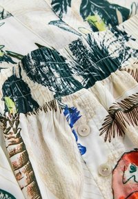 Rochie florală cu frunze verzi și accente albastre pe un fundal alb. Bodice texturat cu pliseuri și două nasturi la talie.