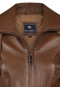 Chaqueta de cuero marrón con cuello alto, cierre de cremallera y textura suave. El forro interior es de un marrón más claro. La etiqueta dice "FELIX HARDY."