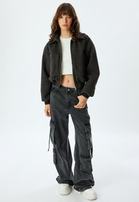 Geknipte donkergrijze fleece jas met twee voorzakken, gecombineerd met losse zwarte cargobroeken met zijzakken en robuuste witte sneakers.