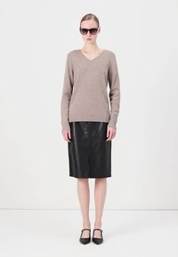 V formos kaklo smėlio spalvos megztinis derinamas su juoda odine sijonu, turinčiu priekinį skilimą, ir juodais balerinų bateliais su čiurnos dirželiu; modelis vilki tamsius akinius nuo saulės.