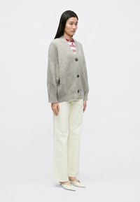 Hall hallast kardigan, millel on V-kaelus ja nööpidega kinnis, kombineeritud triibulise punase ja valge topiga ning kreemjate laiade pükstega.