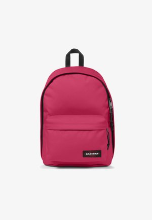 Mochila de tela rosa con un bolsillo delantero con cremallera, cremalleras negras y un lazo para colgar. Textura suave y forma redondeada. Logo de la marca visible.