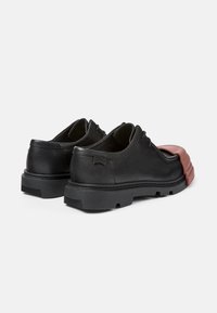 Chaussures en cuir noir avec un détail en caoutchouc rouge contrastant à l'avant. Dotées d'un bout arrondi, d'accents de couture et d'une semelle en caoutchouc texturé.