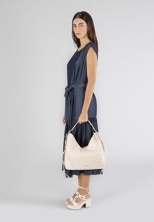 Abito senza maniche di colore blu navy con cintura in vita e gonna a strati; borsa in pelle beige con borchie; sandali platform bianchi con cinturini.