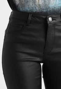 Close-up of a person wearing black high-waisted, fitted leather pants with a button and pocket details.