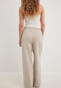 Svetlo bež široke hlače narejene iz mehke tkanine, z elastičnim pasom za udobje. Gladka tekstura, brez vidnih vzorcev ali dodatkov.