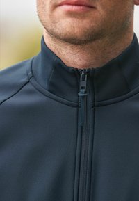 Chaqueta de cremallera azul marino oscuro con un cuello alto, que presenta una textura suave, costuras en contraste y un tirador de cremallera seguro.
