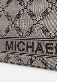 Sac en toile noir avec un motif en losanges et des logos entrelacés, et une étiquette horizontale "MICHAEL" bien en vue en bas.