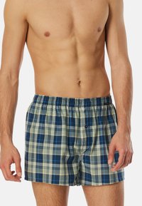 Gelegerde boxershorts in blauw en crème, gemaakt van lichtgewicht stof. Voorzien van een elastische tailleband en een knoopsluiting aan de voorkant.
