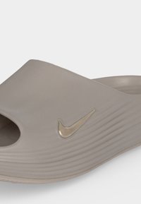 Μπεζ σανδάλι slide της Nike με ανοιχτή μύτη, υφασμένο πάτο και ανάγλυφο λογότυπο Swoosh στο πλάι.