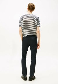 T-shirt a righe a maniche corte con vestibilità casual, abbinato a pantaloni slim-fit blu scuro con tasche posteriori, indossato con scarpe nere.