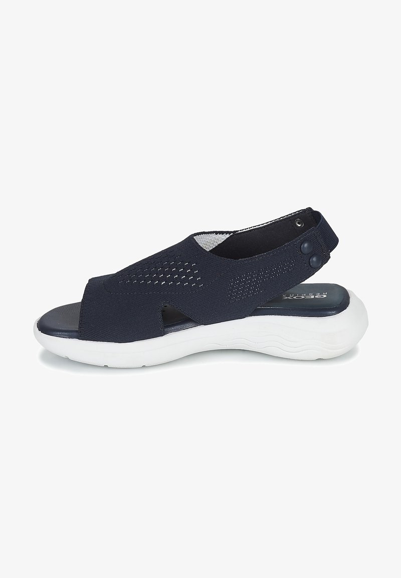 Sandales en tissu bleu marine avec design découpé, semelle texturée blanche, sangle ajustable avec bouton-pression et semelle intérieure rembourrée.