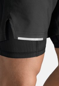 Zwarte sportshorts met een mesh binnenlaag, voorzien van een reflecterend accent op de zoom en een gespleten ontwerp aan de zijkanten voor flexibiliteit.