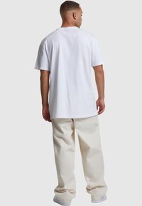 White cotton t-shirt with short sleeves and a relaxed fit, paired with light beige, loose-fitting pants. Simple design, no patterns or accents.