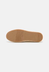 Espadrille sole with a textured rubber bottom, natural jute upper, featuring a woven pattern in a light cream color. Flat and round shape.