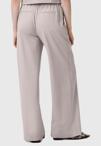 Pantaloni grigi chiari a gamba larga con cintura elasticizzata, dotati di due tasche posteriori e una texture liscia, abbinati a calzature nere a fantasia.