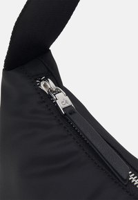 Mustavälinen nylonselkäkassi, jossa on hopeinen vetoketju ja teksturoitu hihna. Vetoketjussa on pieni brändätty yksityiskohta sen vieressä.