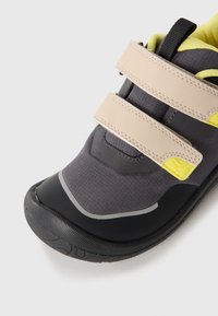 Chaussure de sport à sangle Velcro en tissu gris foncé avec des accents jaunes et une semelle en caoutchouc noir. Comprend un col rembourré et un capuchon de toe texturé.