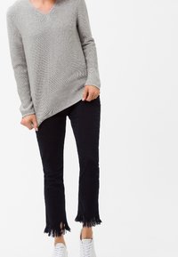 Suéter gris de punto texturizado con escote en V y mangas largas, combinado con pantalones negros con dobladillos con flecos. Zapatillas blancas completan el conjunto.